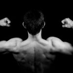 Black and white photo of a muscular man flexing arms against a dark background.