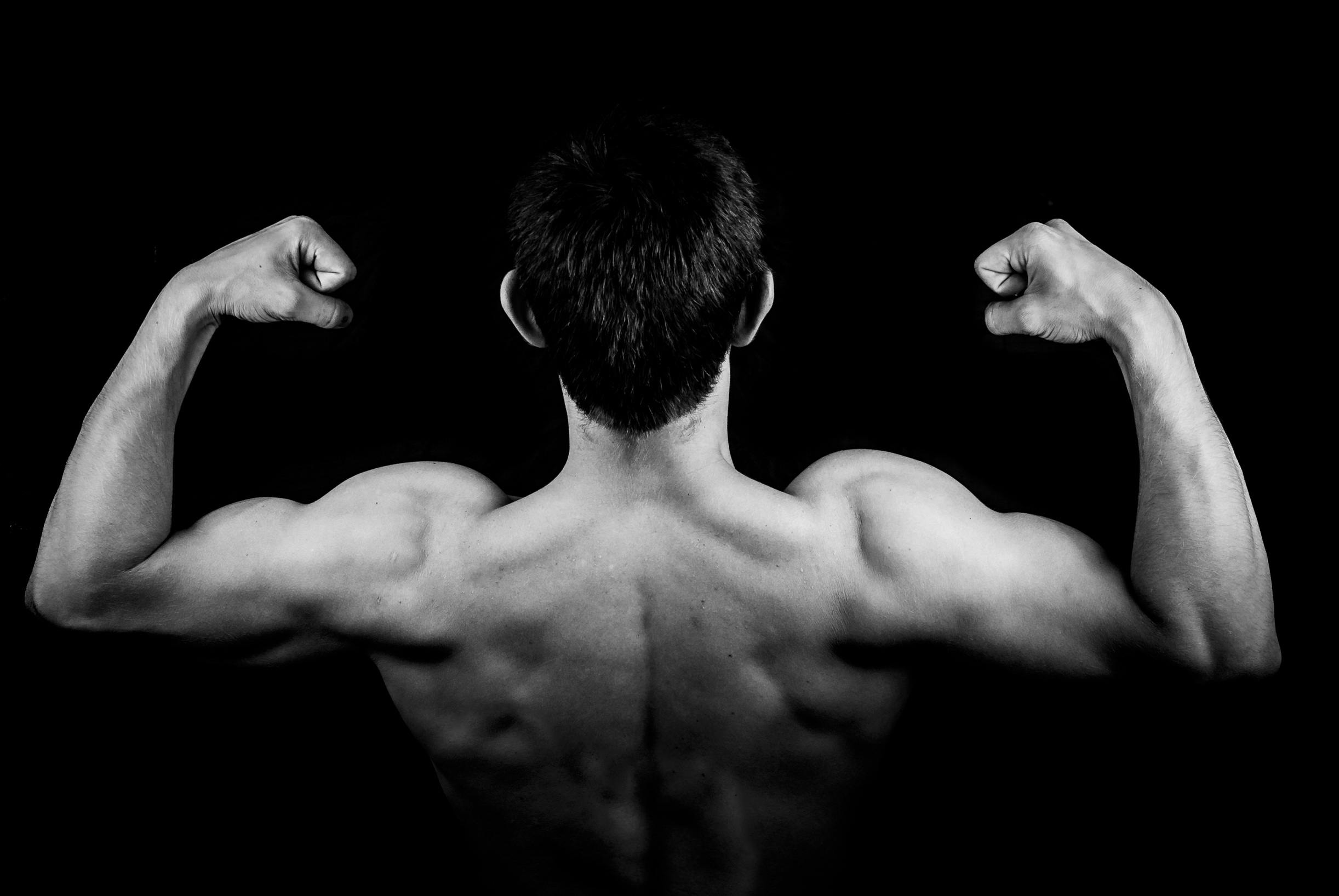 Black and white photo of a muscular man flexing arms against a dark background.